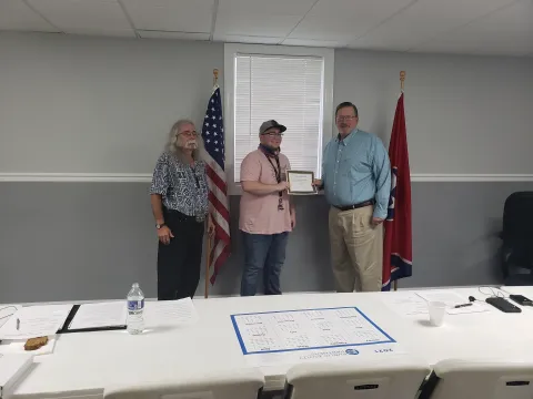 Picture of three males with the one in the middle receiving a certificate for a scholarship for high school achievement