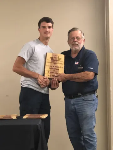 A teenager and a man.  The man is handing the teenager a plaque.