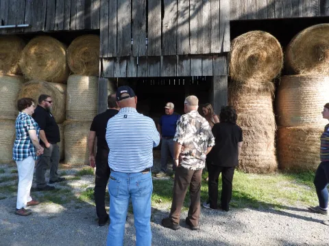 In front of a hay barn one man is telling others about the farm.