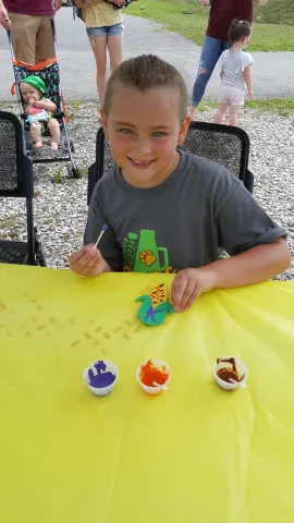 Young girl smiling and showing the refrigerator magnet shaped like corn that she painted.