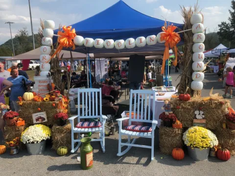 picture of Rocky Top Award winner for best portrayal of the festival theme, More Fiddlin' Around, was A& B Bookkeeping and Tax Service. Picture has two white rocking chairs in front of a banner made of pumpkins that say More Fiddlin' Around.  The rocking chairs are surrounded by mums in washtubs with a fiddle displayed on haybales.