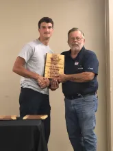 A teenager and a man.  The man is handing the teenager a plaque.