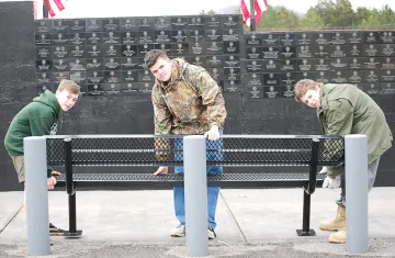 Zarian Stephens (center) receives an assist from scouts Robert Cocran (L) and Camden Batchellor (R) to install a bench at the Veterans Wall in Wilson Park.